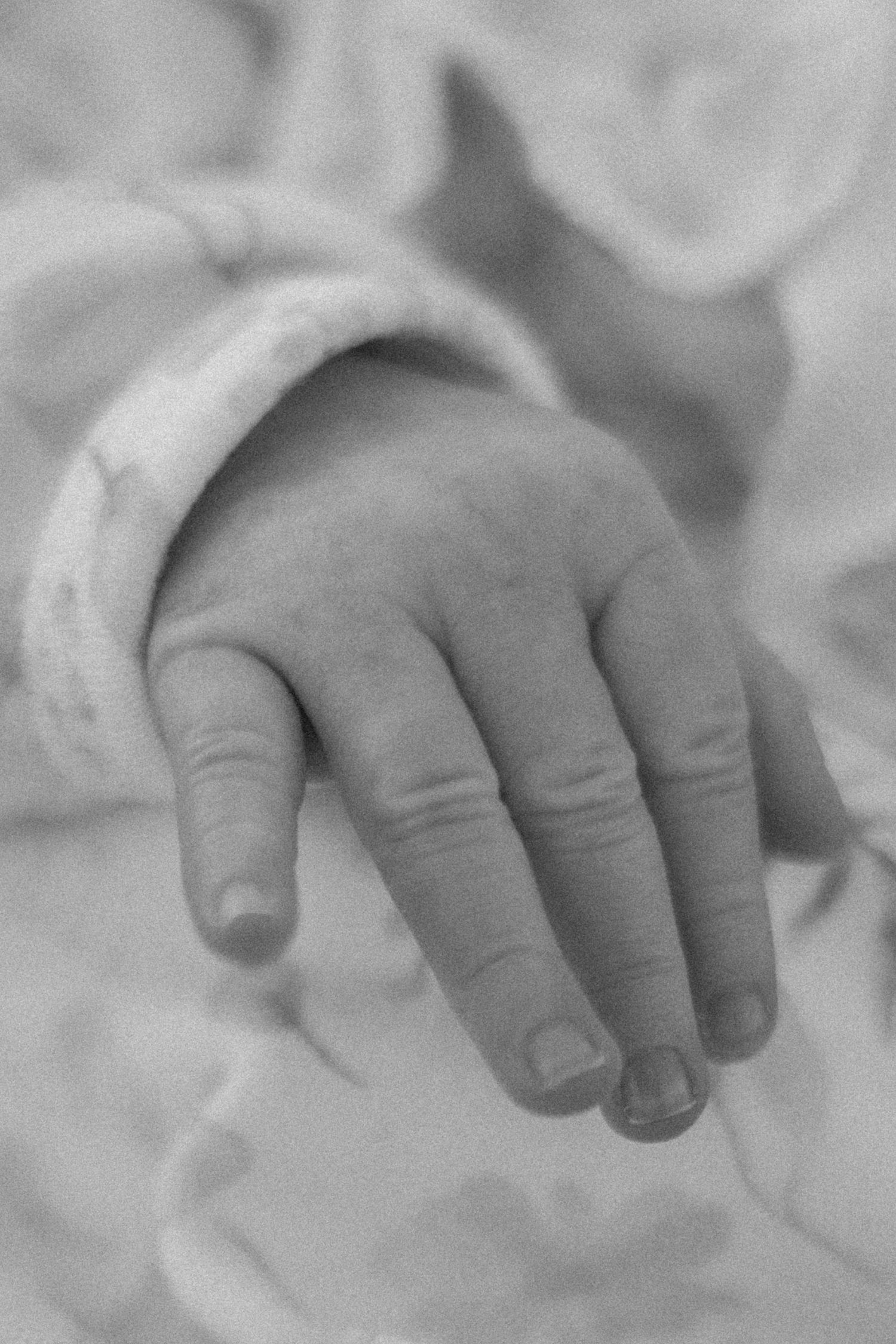 Black and white close-up of a newborn baby's tiny hand resting gently on soft fabric with a delicate sleeve cuff.